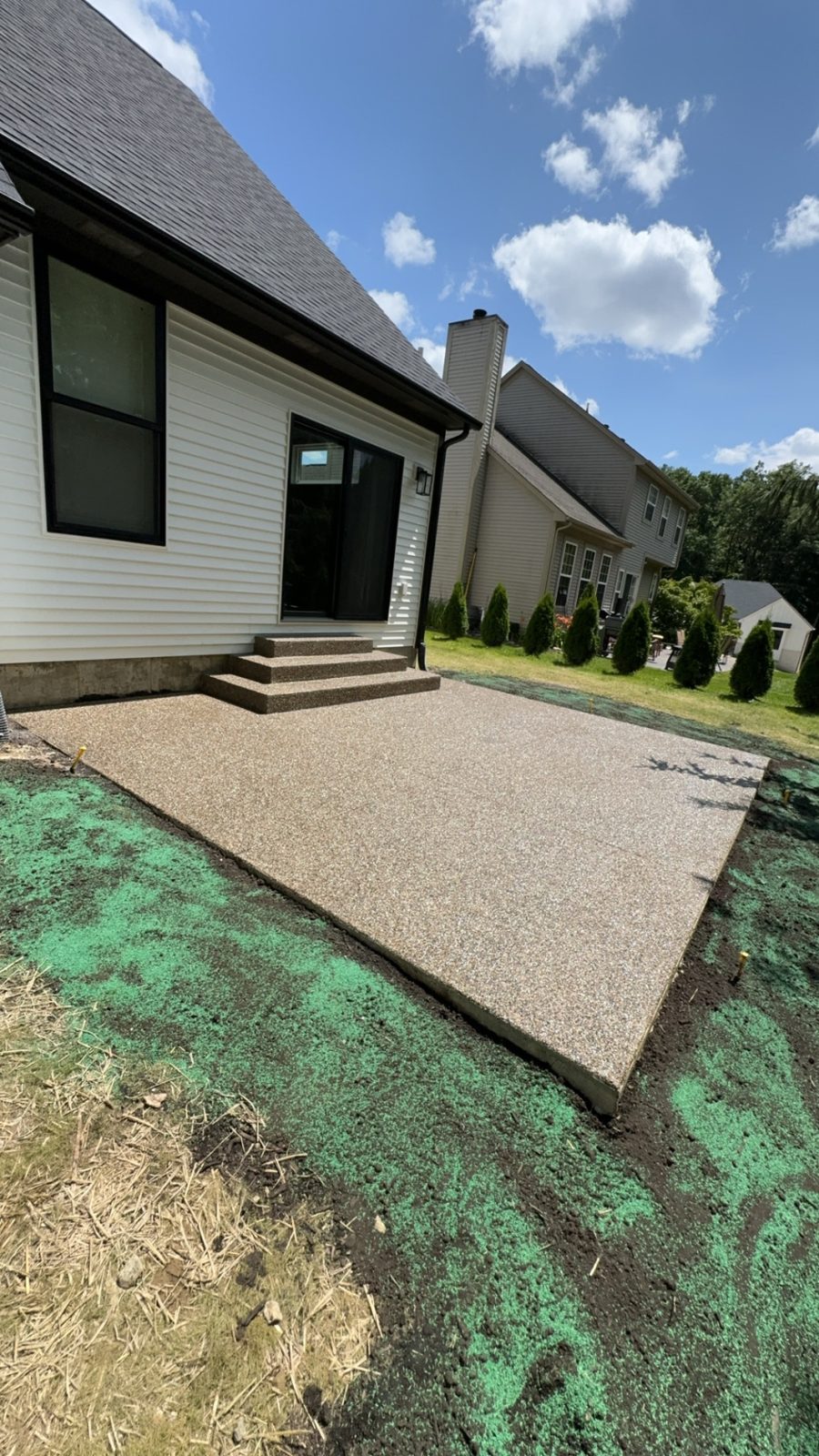 Large exposed aggregate concrete patio with matching steps behind a brick Southeast Michigan home